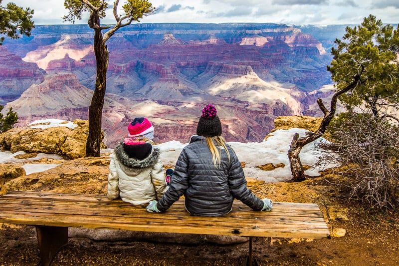 two girls sitting on bench looking at grand canyon views. 