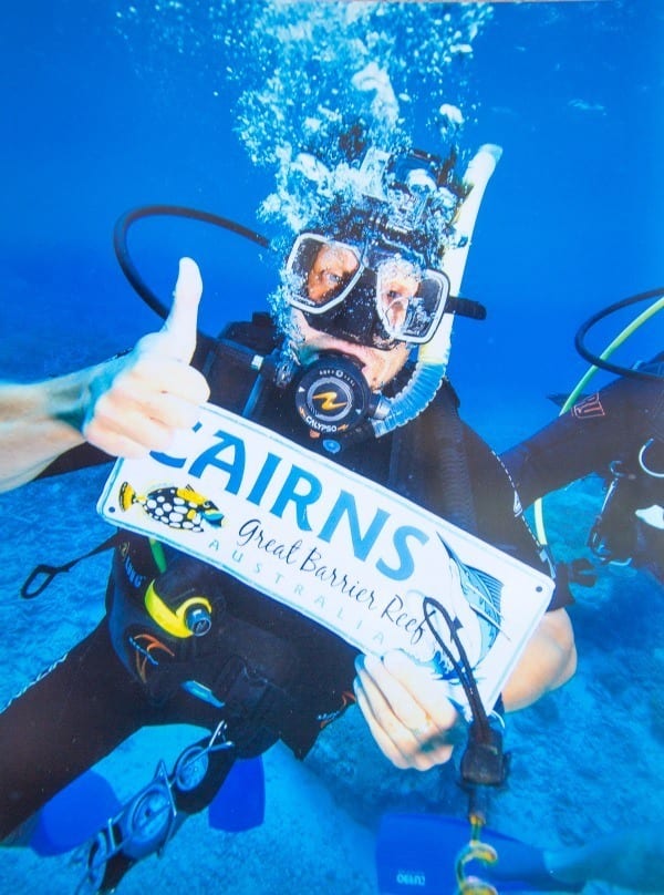 man holding up cairns sign under water while scuba diving