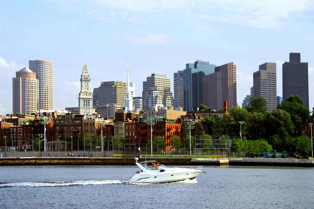 Luxury white boat cruising on the Charles River with the Boston skyline in the background featuring notable buildings like the Custom House Tower