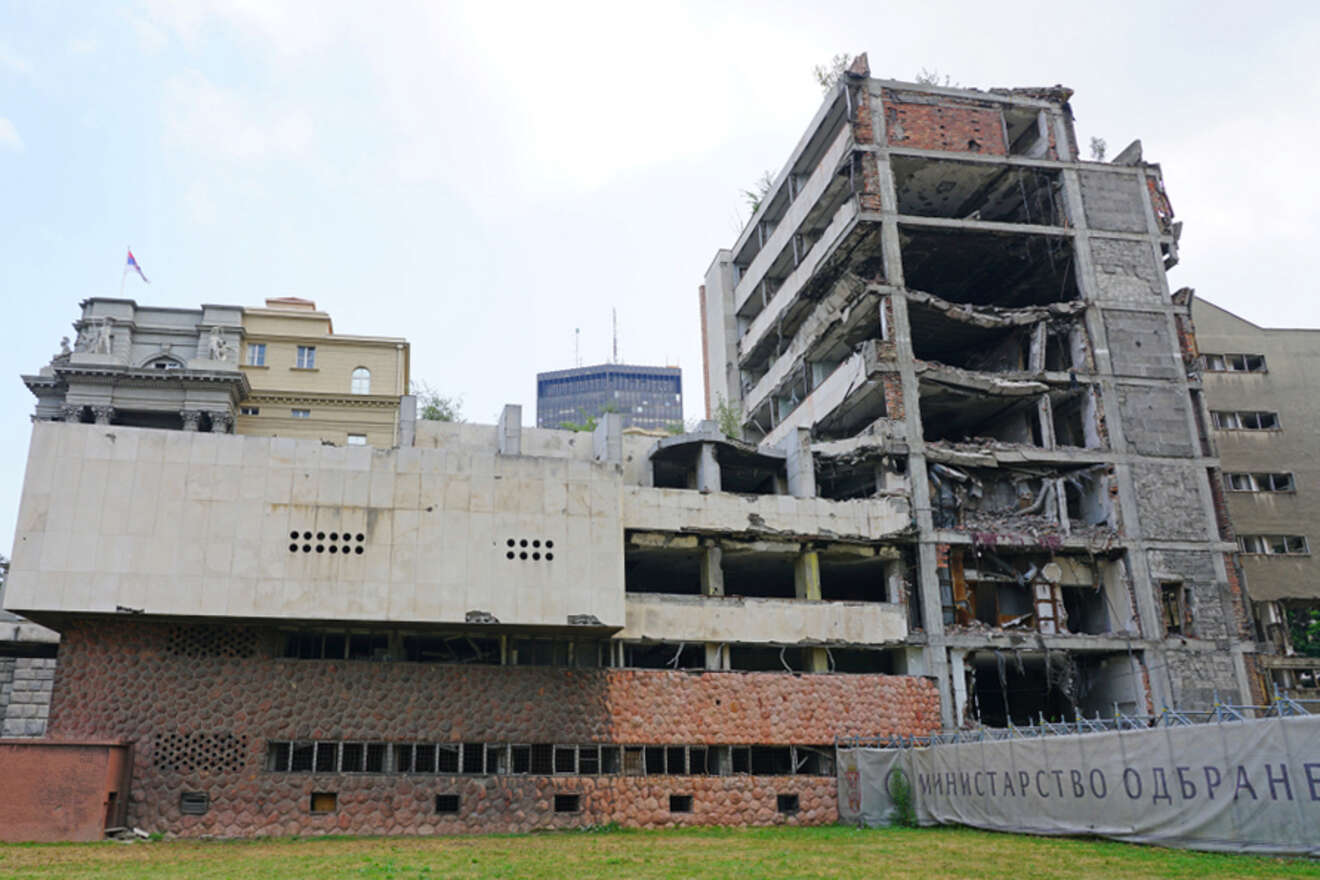 A damaged building in Belgrade with visible destruction on its facade, surrounded by a fence, a remnant of the NATO bombing.