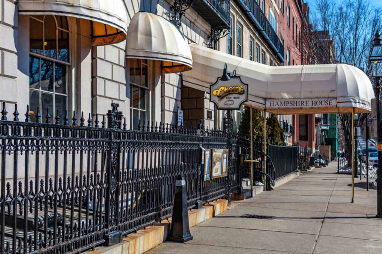 Exterior of the iconic Cheers bar at Hampshire House in Boston, with its recognizable sign and awning, set against a backdrop of brick buildings