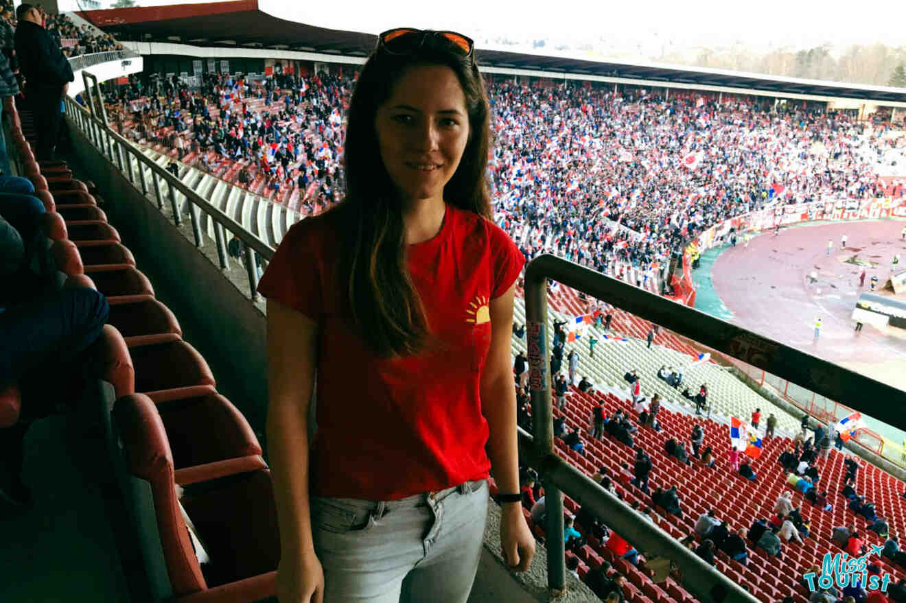 The writer of the post stands at a football stadium, representing Belgrade's passionate football culture with fans filling the stands