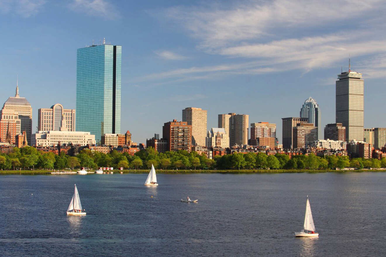 Pleasure boats sailing on the Charles River with the Boston skyline in the background, showing the Prudential Center and Hancock Tower on a sunny day