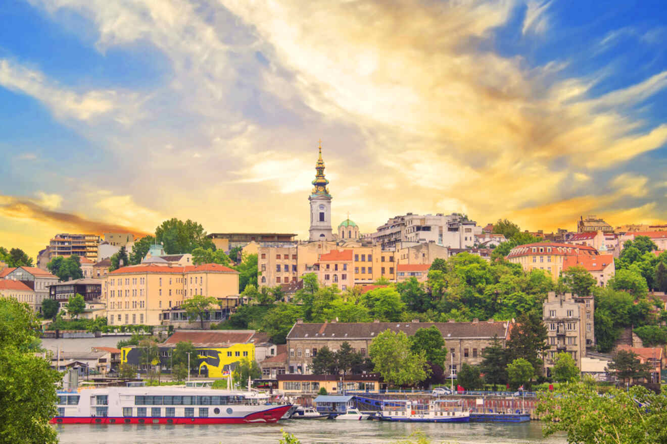 Scenic view of Belgrade's skyline at sunset with the silhouette of St. Michael's Cathedral standing above the city, and the Sava River bustling with boat traffic