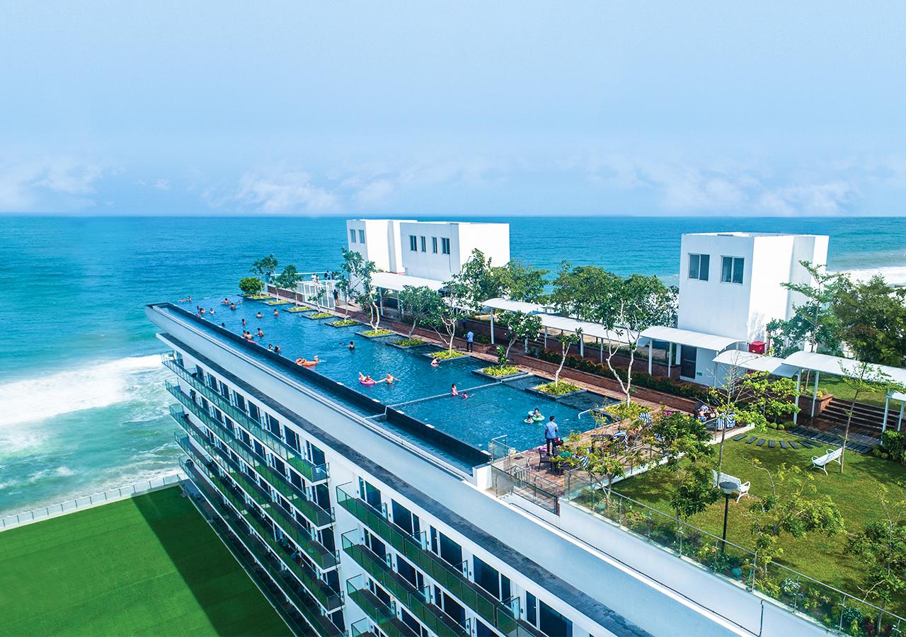 Guests enjoy an infinity pool on a rooftop terrace overlooking the ocean, with the edge of the pool creating a seamless visual extension into the blue sea under a clear sky, offering a luxurious and tranquil leisure experience.