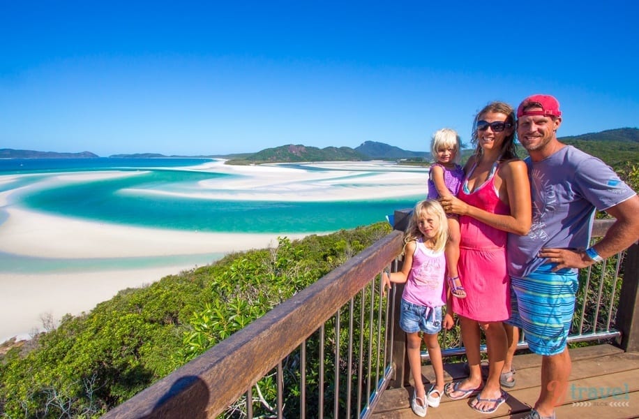 family posing in front of vista of swirling white sands and turquoise water of whitehaven beach