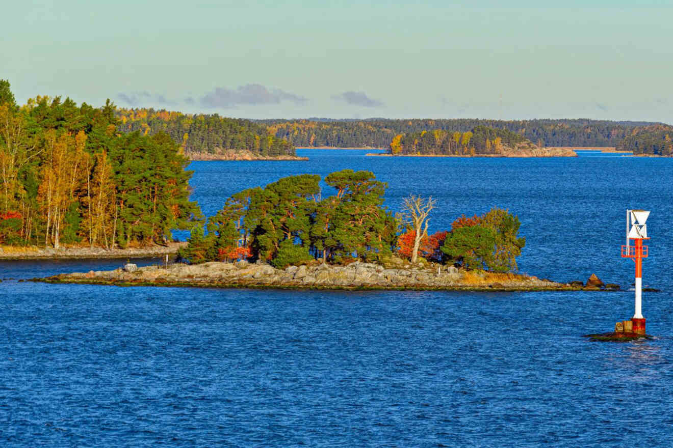 Autumn colors touching the trees on a small island in the Turku Archipelago, with calm sea waters and a navigation mark in the foreground