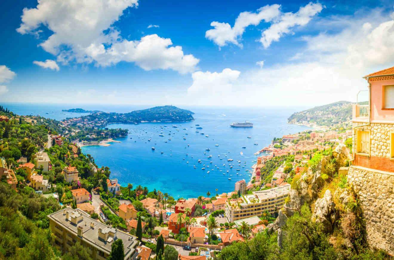 Aerial view of the coastal landscape near Villefranche-sur-Mer, France, with densely clustered houses, green hillsides, and the azure Mediterranean Sea