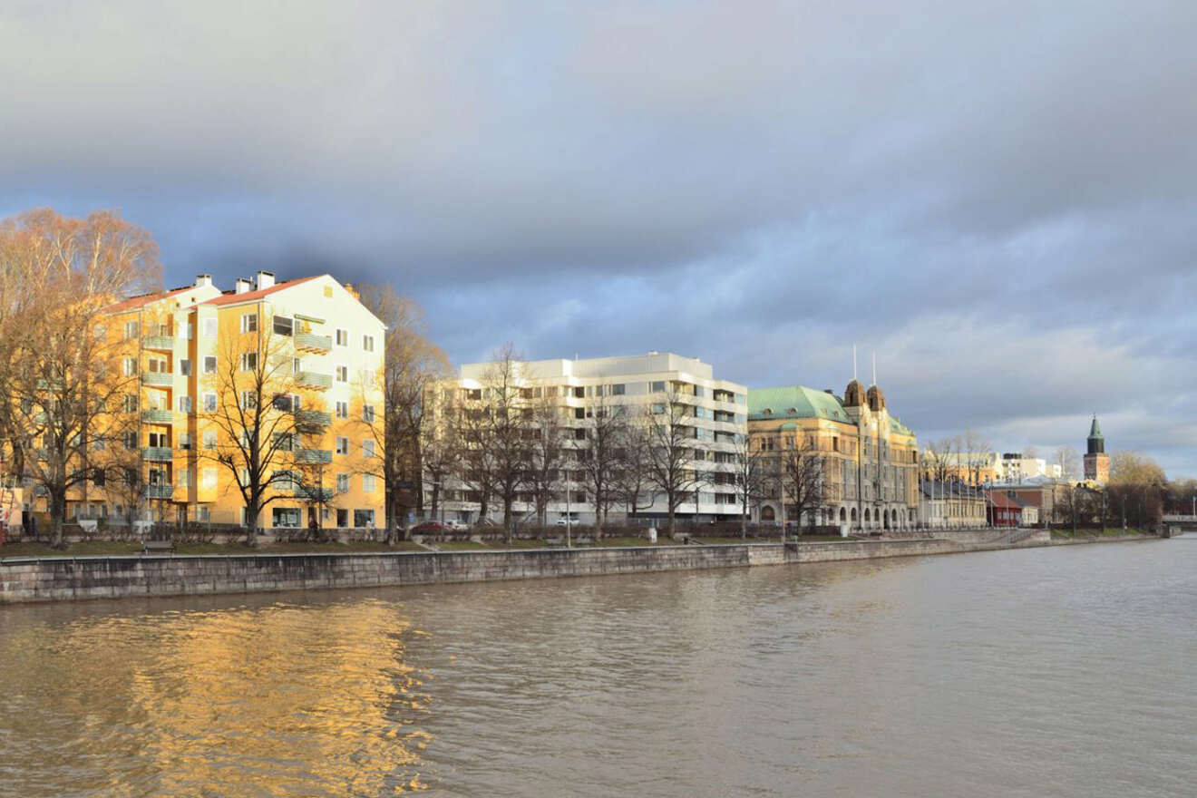 Riverfront apartment buildings basked in golden sunset light, reflecting off the Aura River in Turku, with a clear sky above