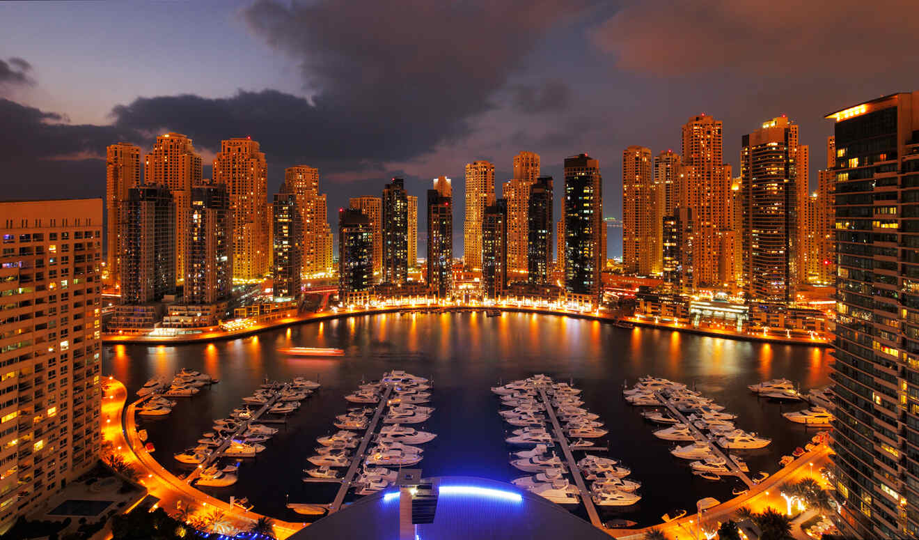 Twilight view of a bustling marina in Dubai with illuminated skyscrapers and docked yachts