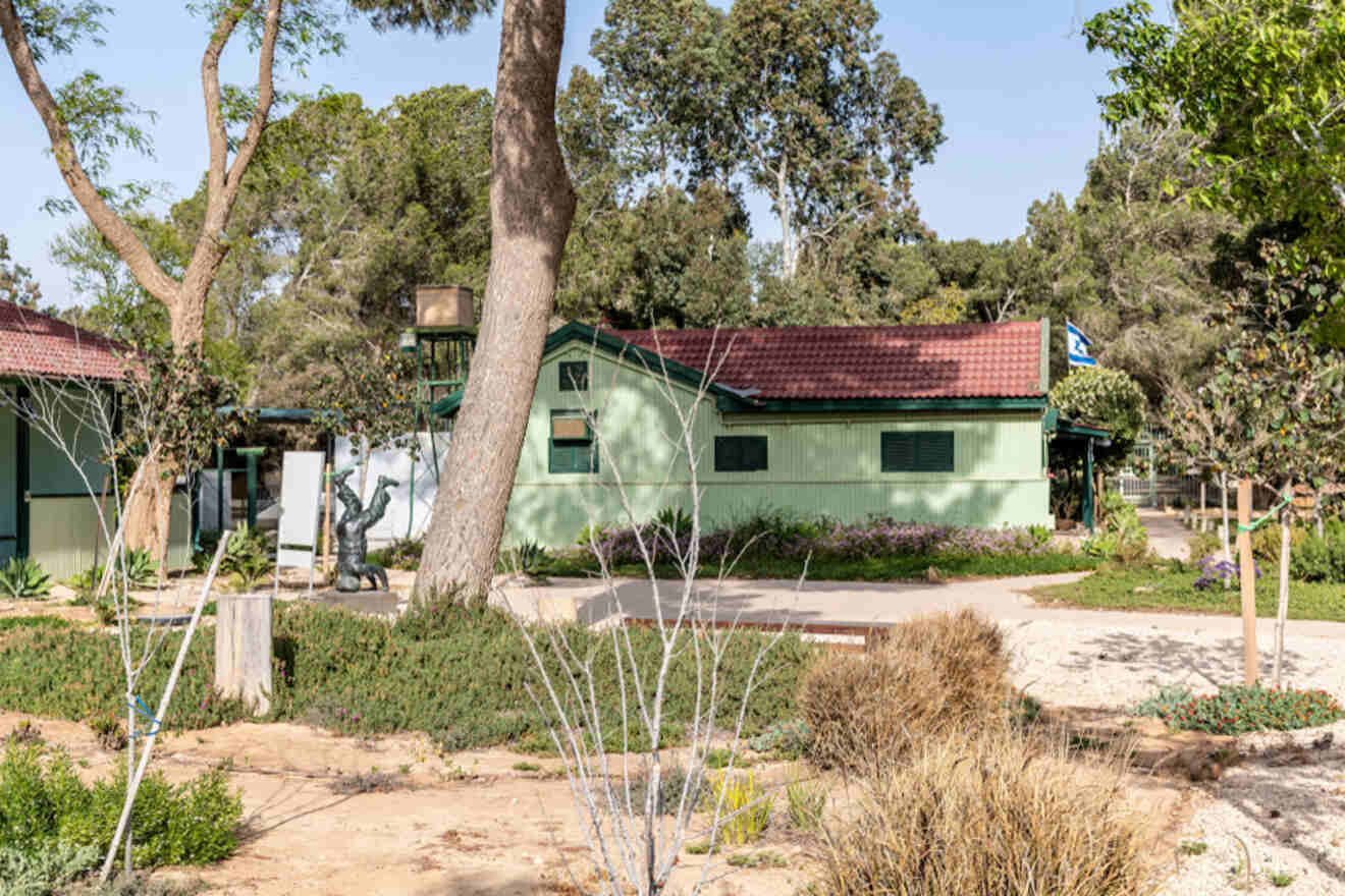 A serene green space with a historic green house, sculptures, and tall trees, displaying a peaceful setting for relaxation