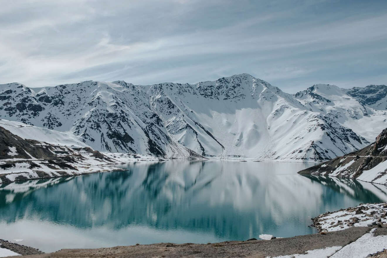 Stunning landscape of Cajon del Maipo, Chile, with a tranquil lake reflecting snow-capped Andean mountains under a clear sky