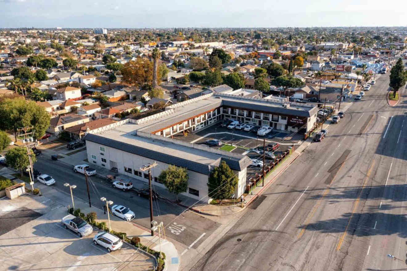 Aerial view of a busy intersection in Lakewood, Long Beach, with a clear view of the surrounding residential area, streets lined with cars, and a mix of commercial buildings under the late afternoon light