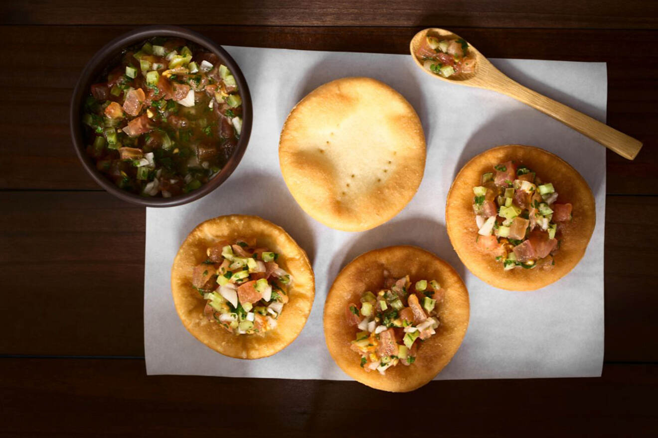 Overhead shot of traditional Chilean dishes, including sopaipillas and a bowl of pebre, on a wooden table