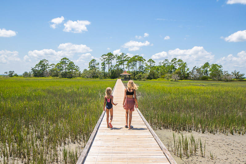 girls walking down boardwalk over marshlands