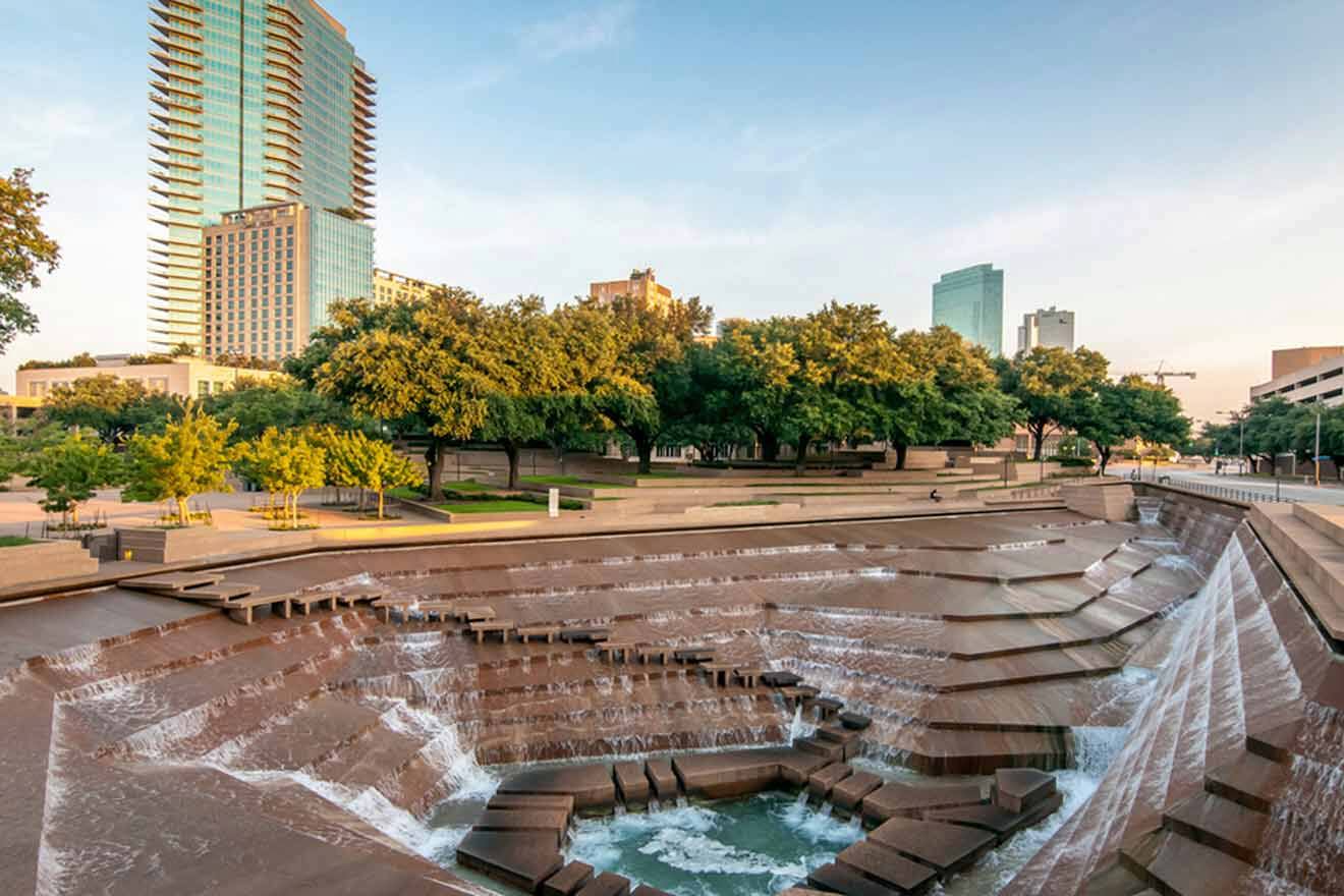 A cascading urban water feature in a public space, surrounded by trees and modern buildings, providing a tranquil setting in the city.