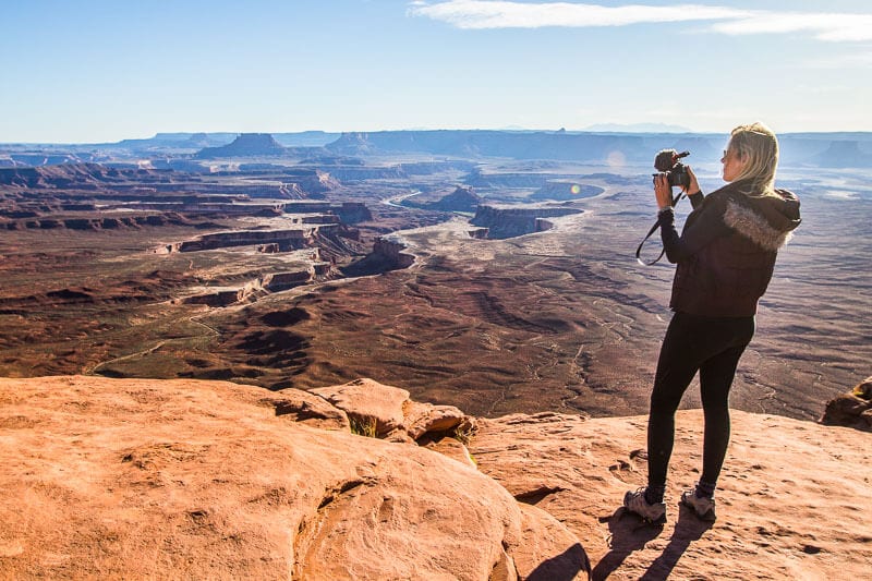 woman taking photos of river running through canyon