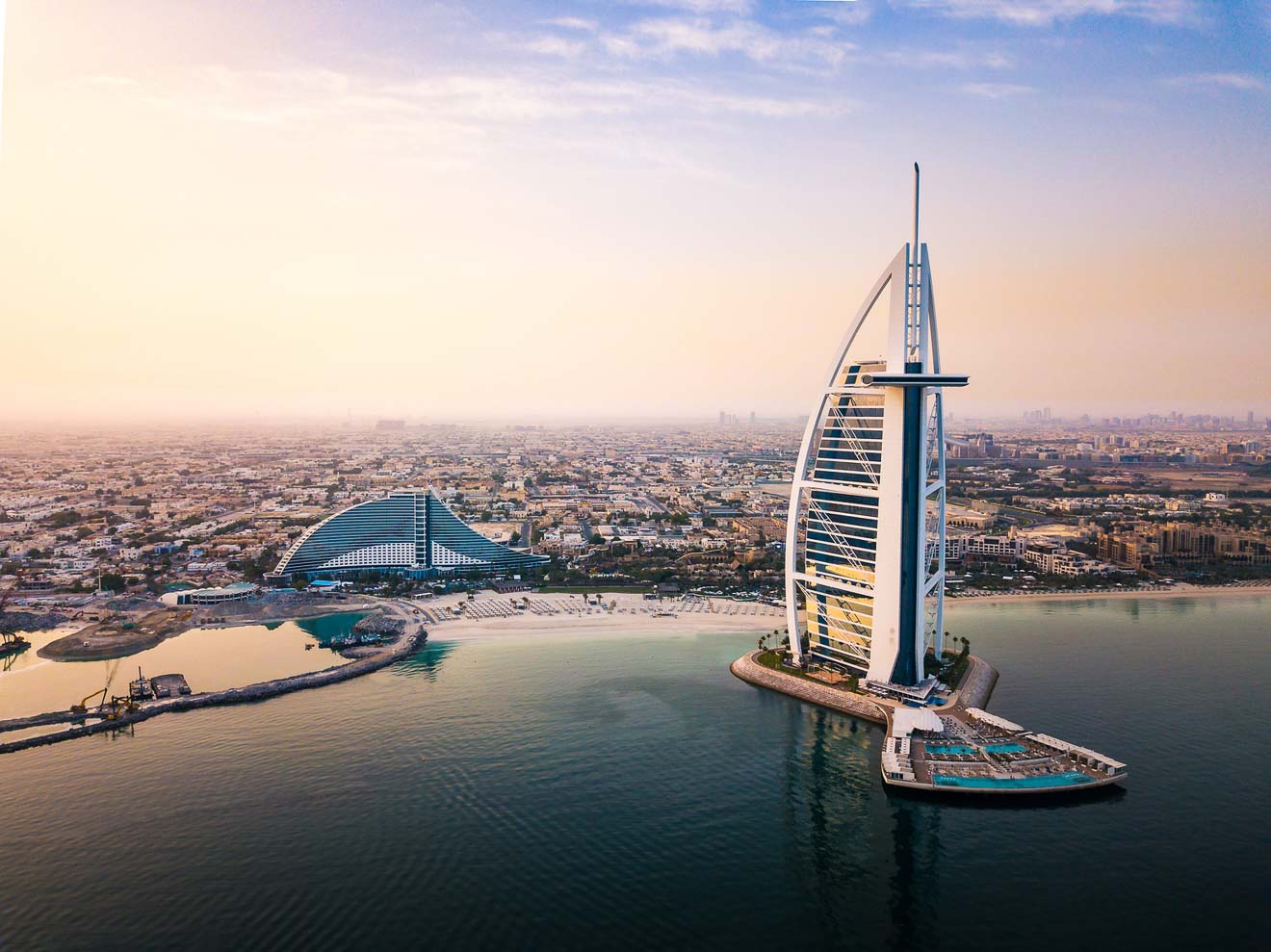 Iconic Burj Al Arab hotel in Dubai captured at sunset, with its sail-shaped structure overlooking the Persian Gulf.