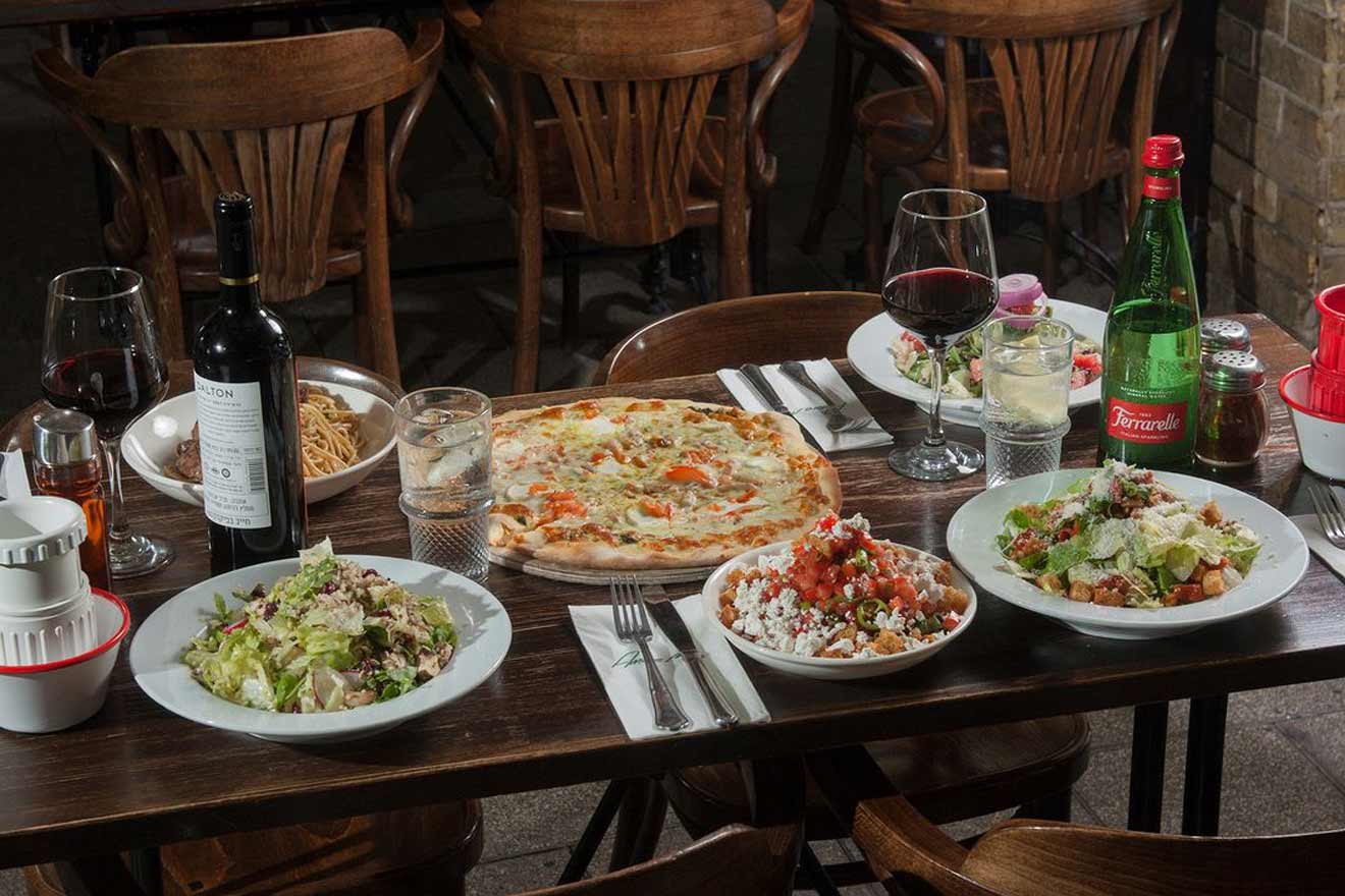 A rustic table filled with a variety of Italian dishes, including pizza, pasta, salad, and wine, representing a traditional Italian meal in a cozy restaurant ambiance